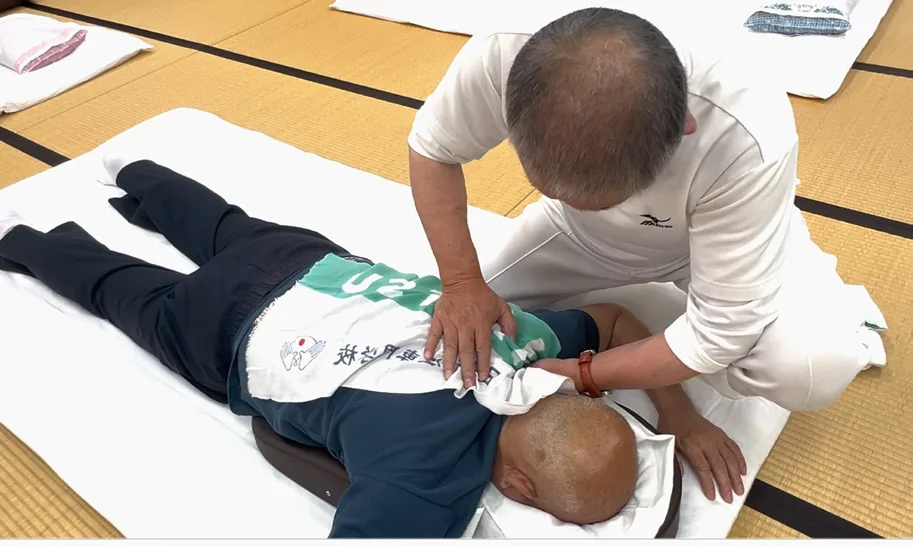 片手で肩甲骨を固定しながら肩上部を指圧する手技